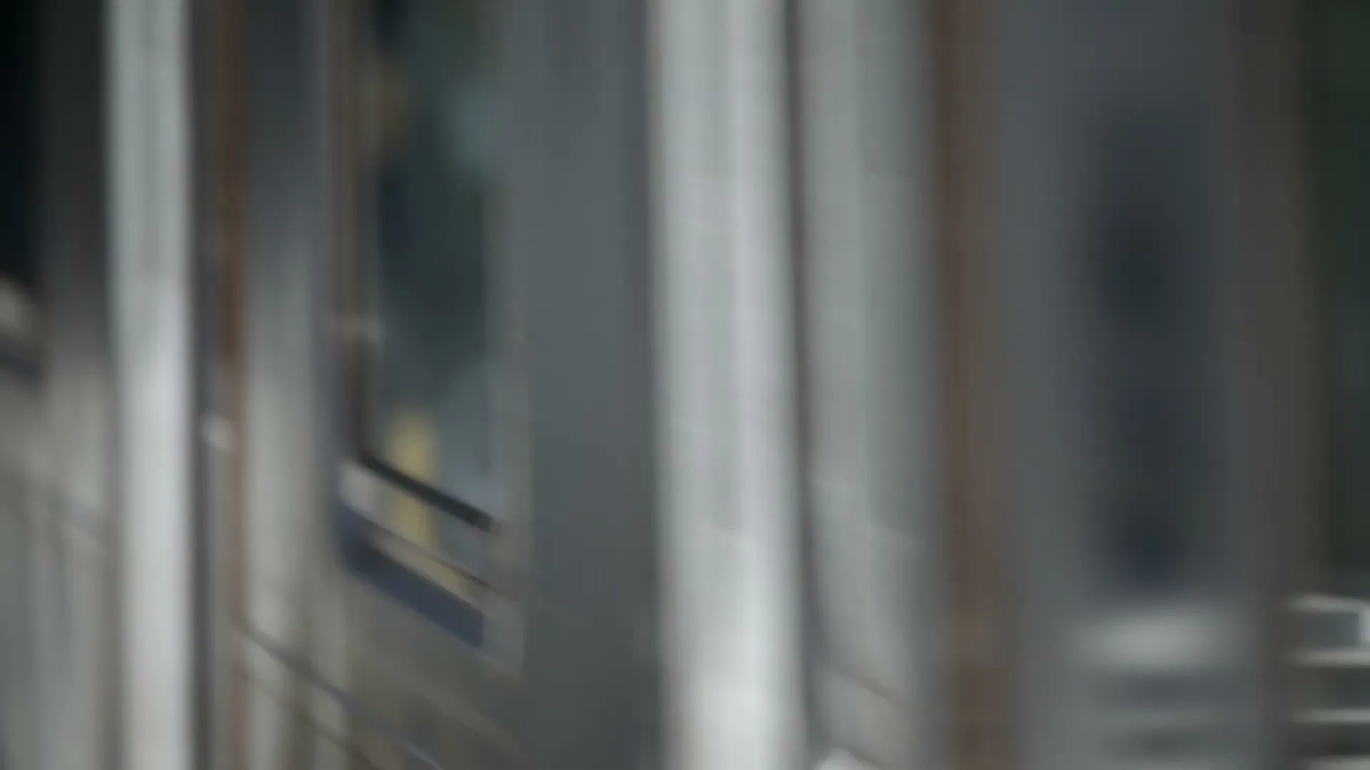 A blurry shot of a moving subway train with its windows and doors visible, passing by quickly in an urban setting.