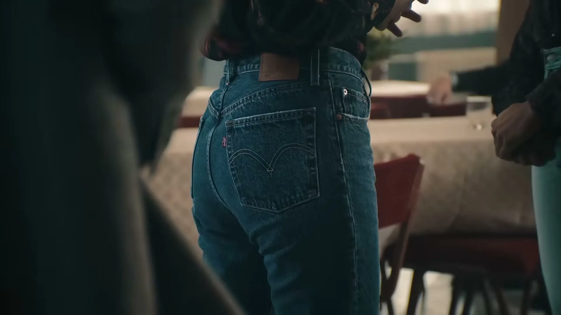 A person wearing blue Levi's jeans stands with their back to the camera, showing the iconic stitching and patch, in an interior setting.