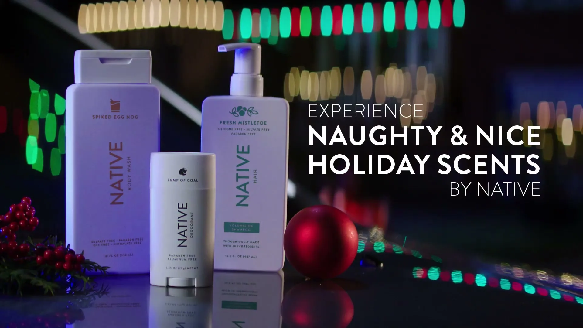 Three Native brand holiday-themed personal care products are arranged on a reflective surface with festive lights in the blurred background.
