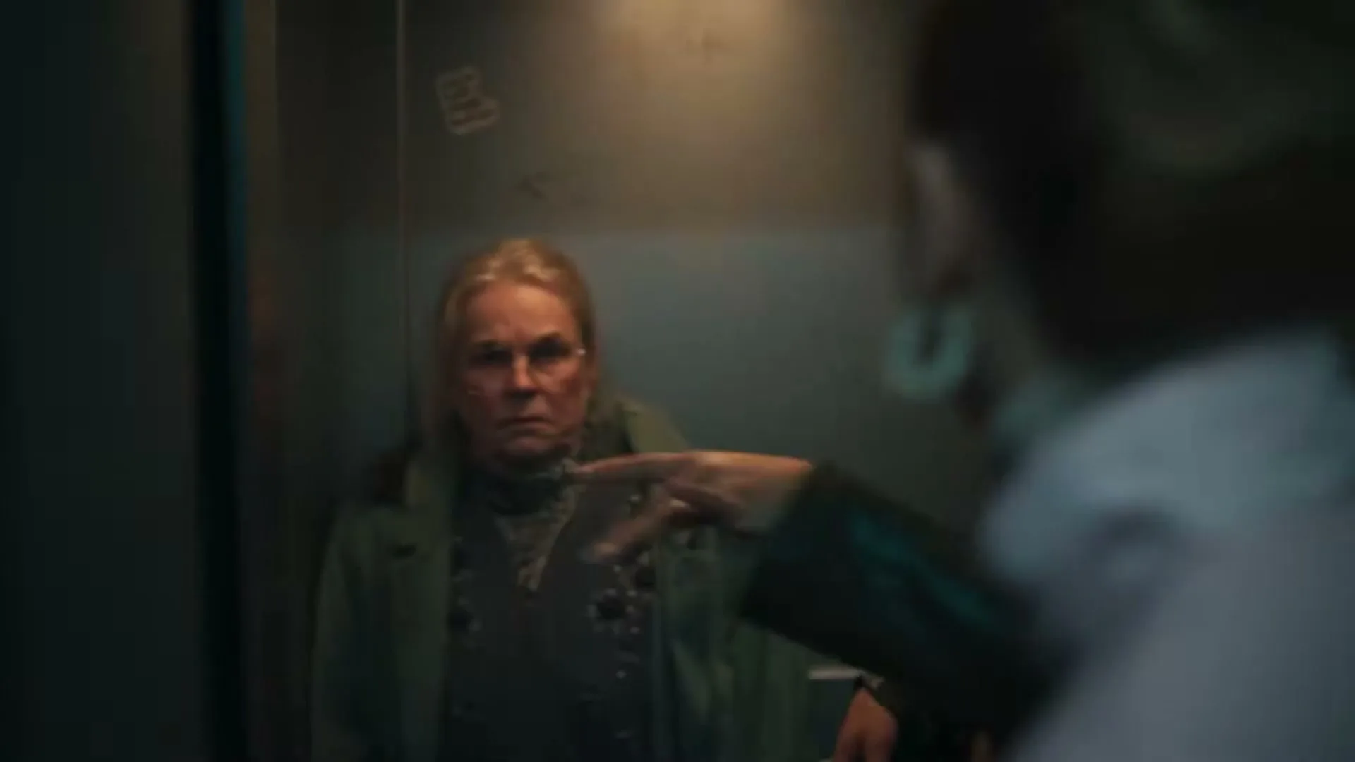 A woman with blonde hair and glasses looks distressed as she is pushed into a dark, confined space by an unseen person.