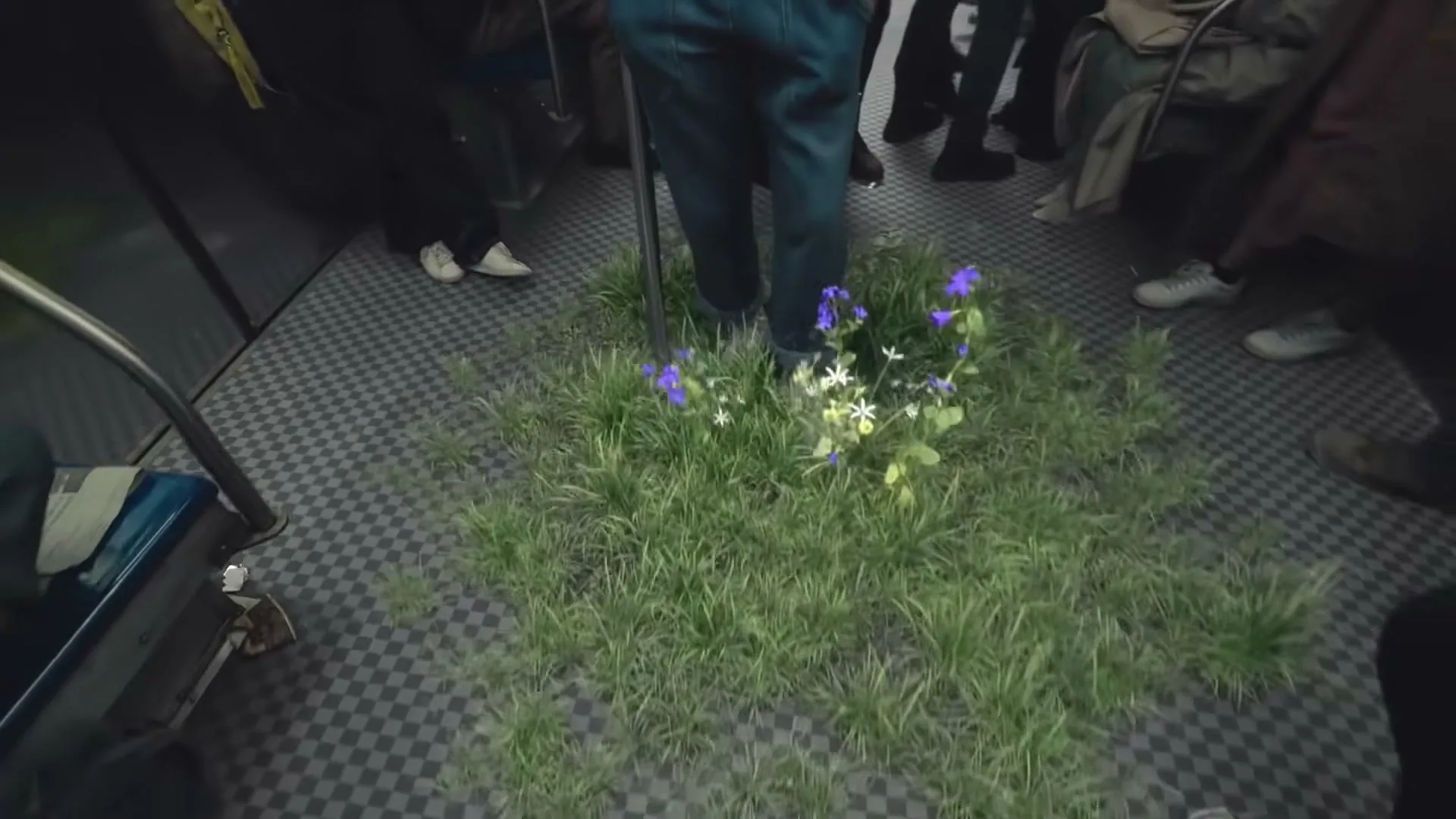 A young woman in a varsity jacket walks through a subway car, as grass and flowers magically grow on the floor around her and other passengers.