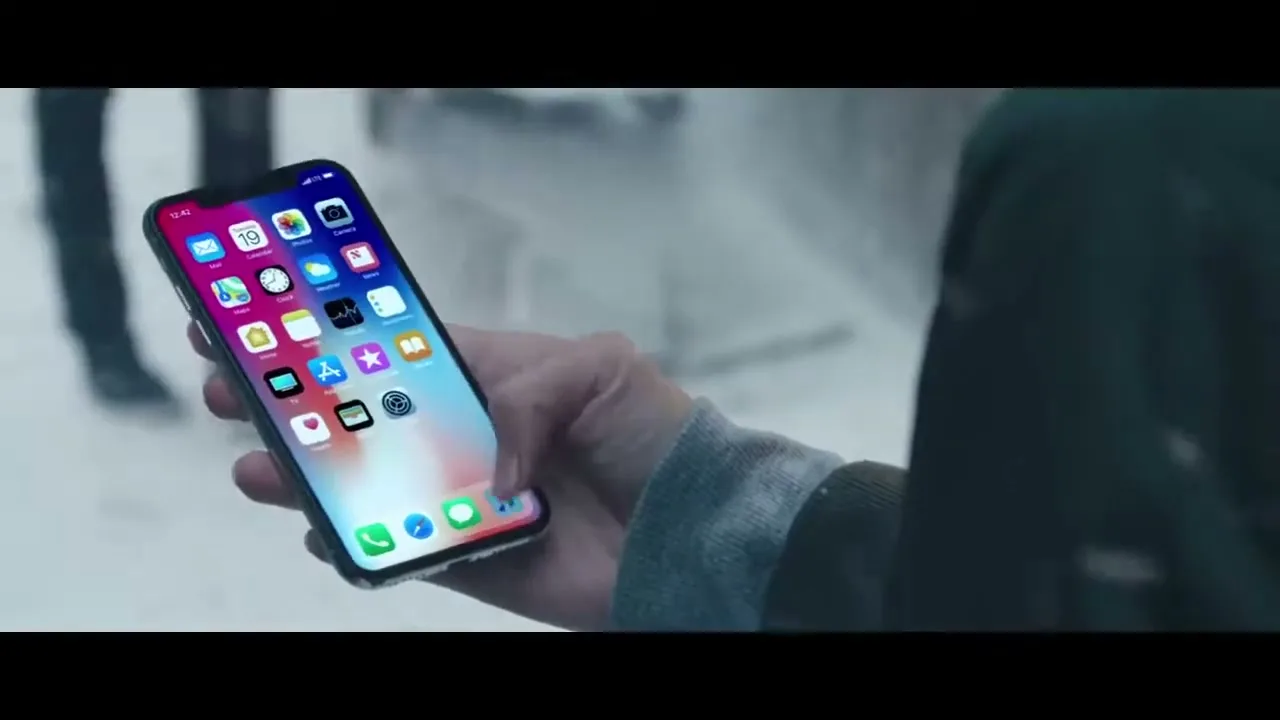 A person's hand holds an iPhone X, unlocking it and then playing music by Sam Smith, in a snowy outdoor setting.