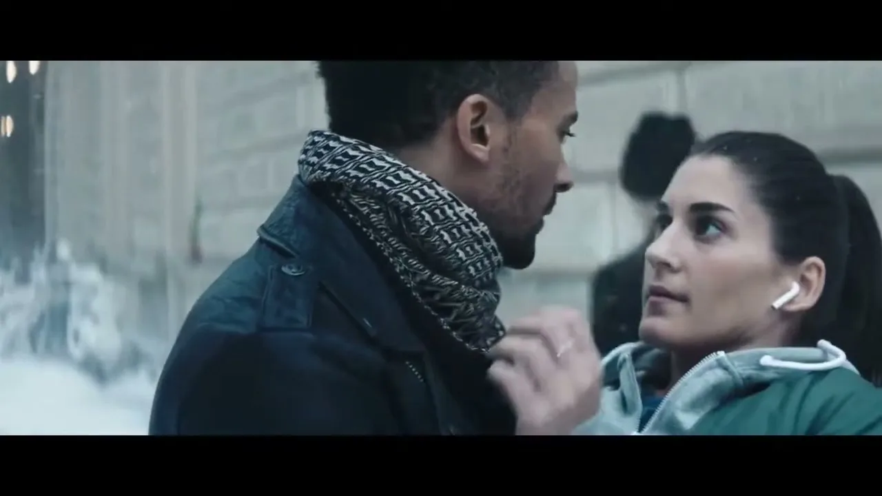 A man and a woman, both in their 20s, look at each other while dancing in a snowy city street.