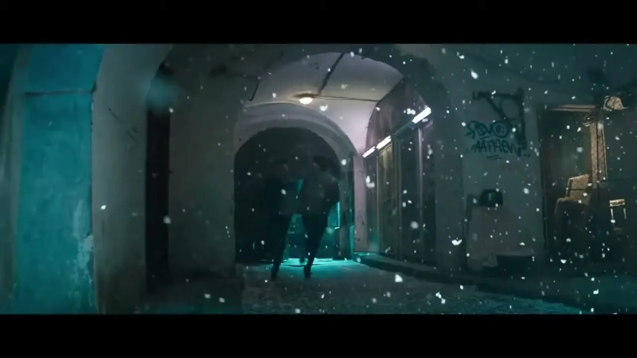 Two people, a male and a female, run through a snowy, arched alleyway at night, illuminated by blue and white lights.