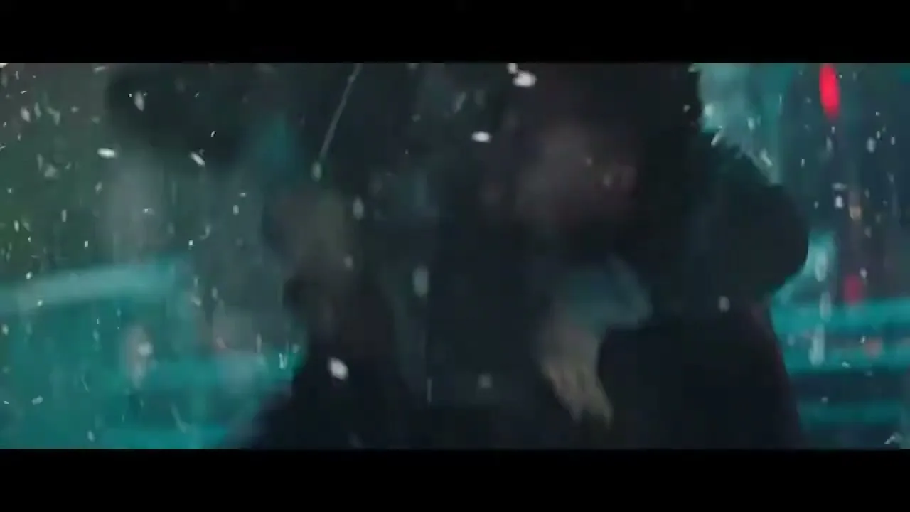 A young man and woman dance closely in the rain at night, illuminated by streetlights, with water splashing around them.