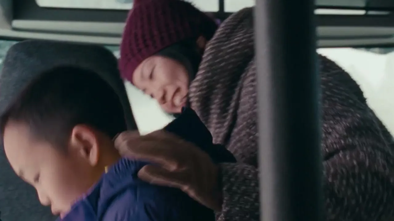 A young Asian woman in a maroon beanie and a brown coat helps a young Asian boy in a blue jacket off a bus.