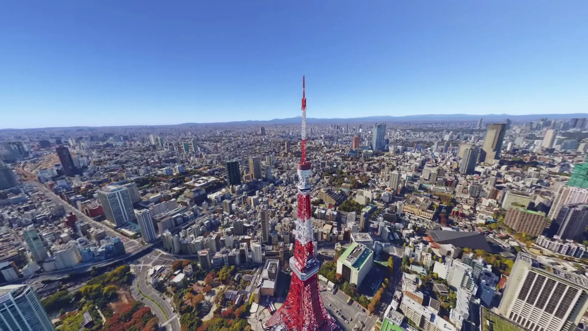 An aerial view of Tokyo, Japan, with the iconic red and white Tokyo Tower prominently featured in the center, surrounded by a sprawling cityscape under a clear blue sky.