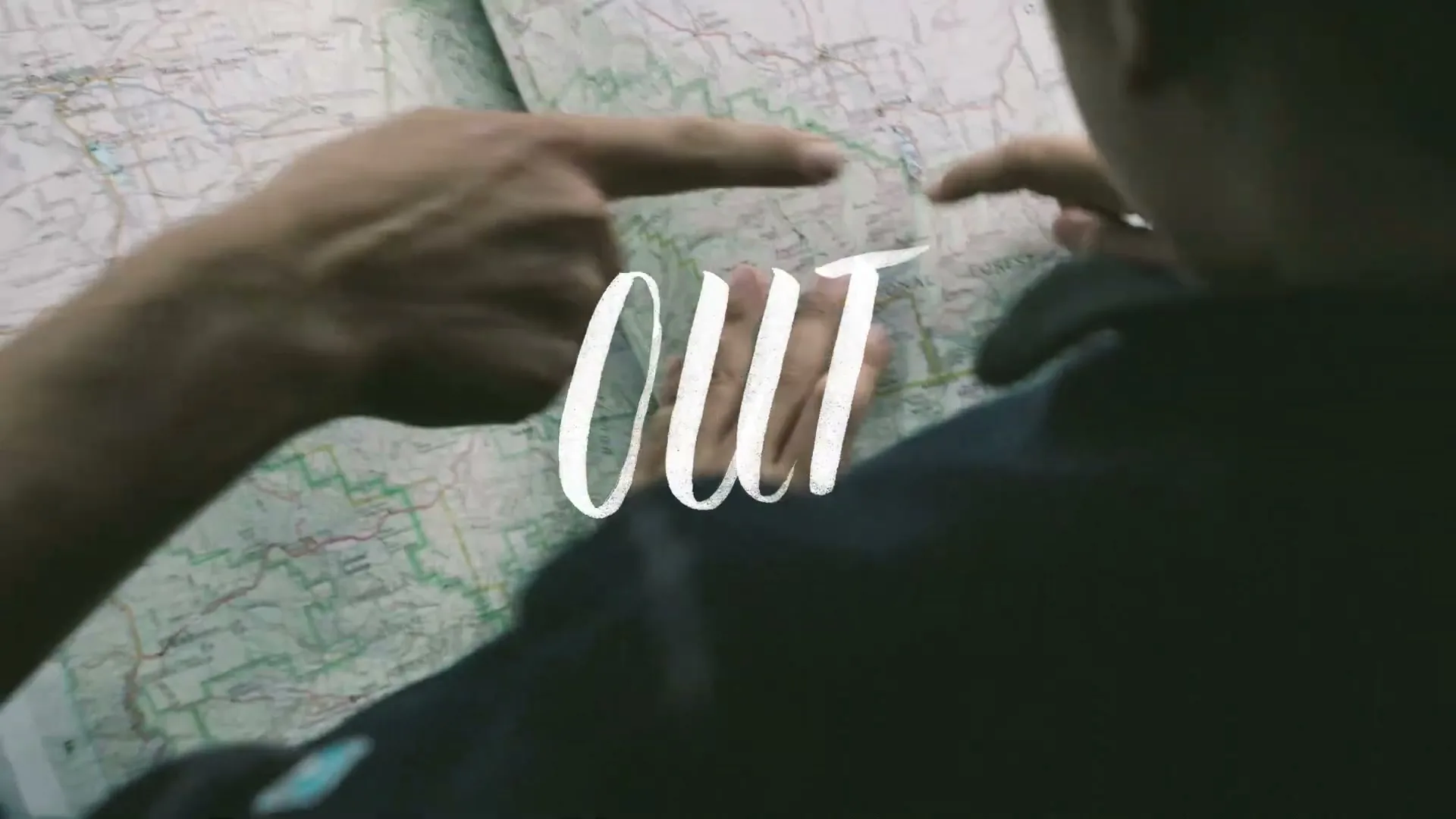 Two people's hands point at different locations on a large paper map, planning a trip together.