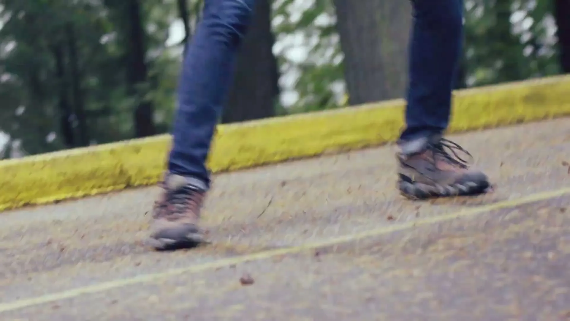 A man in a blue beanie and a grey jacket runs joyfully in the rain on a paved road surrounded by trees.