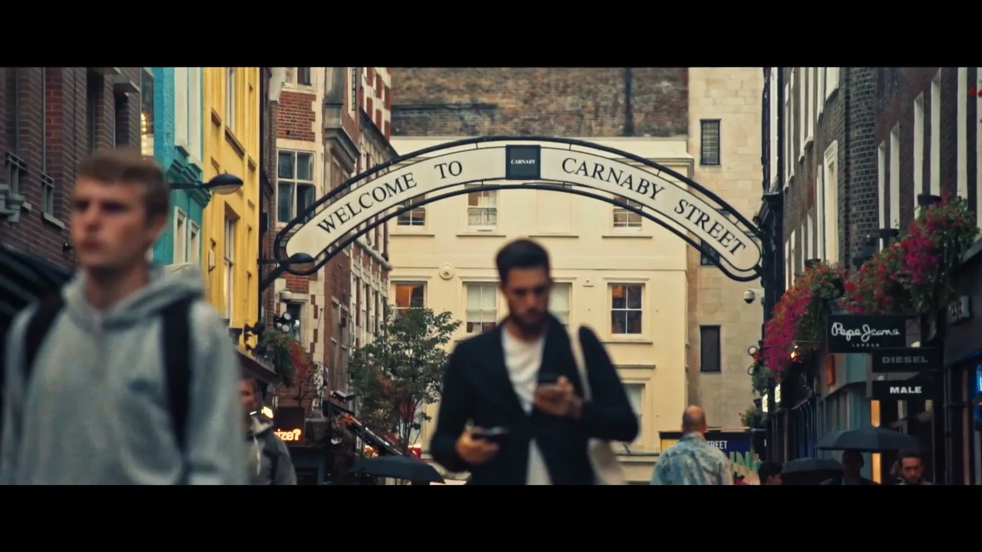A "Welcome to Carnaby Street" archway stands over a busy street with pedestrians walking by, some out of focus in the foreground.
