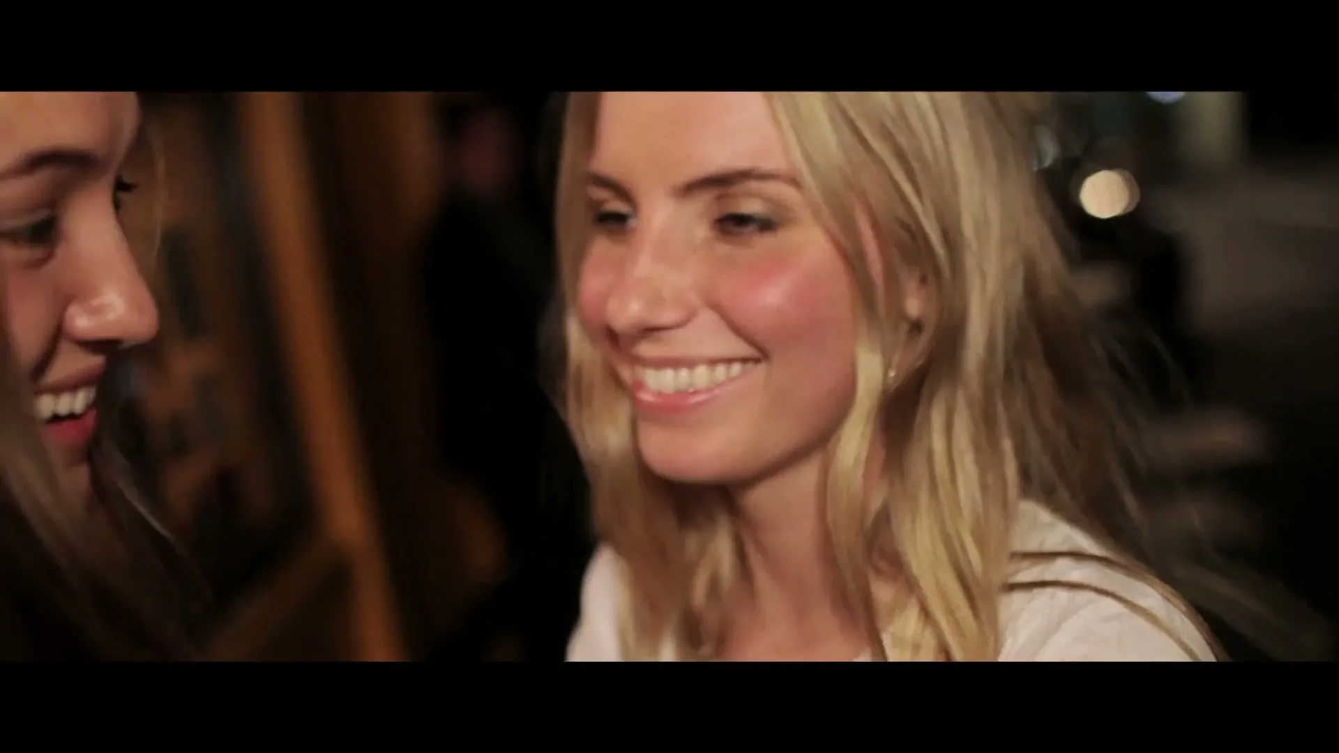 Two young women, one with dark hair and one with blonde hair, smile and laugh together at night on a city street.