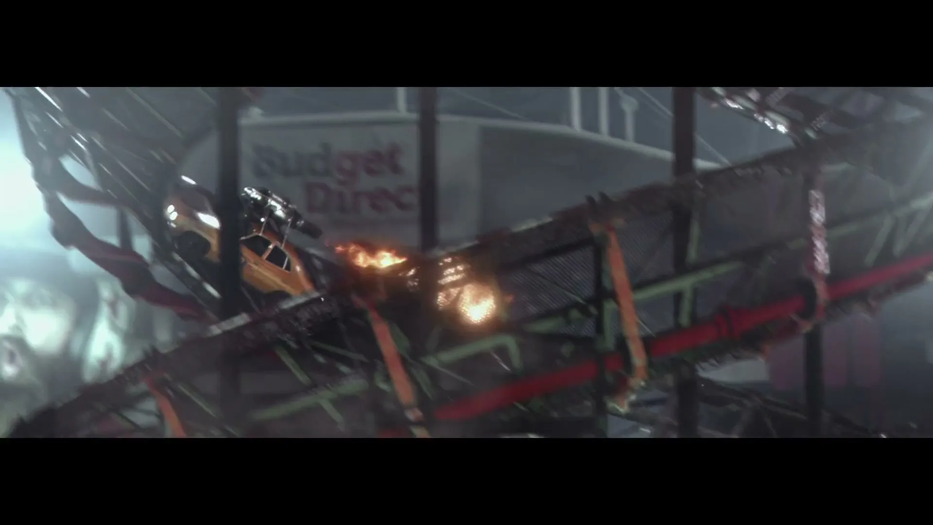 A yellow stunt car with a black stripe drives up a ramp, sparks flying, then crashes and burns in a stadium at night.