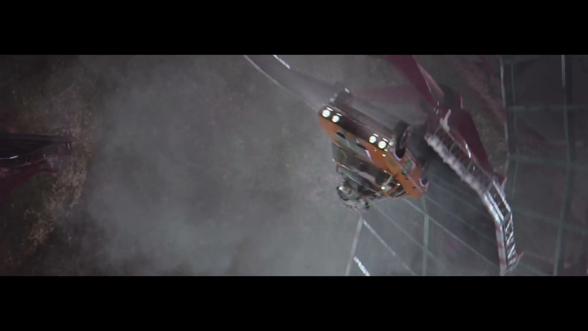An orange car with a green stripe is seen from above, upside down, crashing into a metal barrier, creating a cloud of dust.