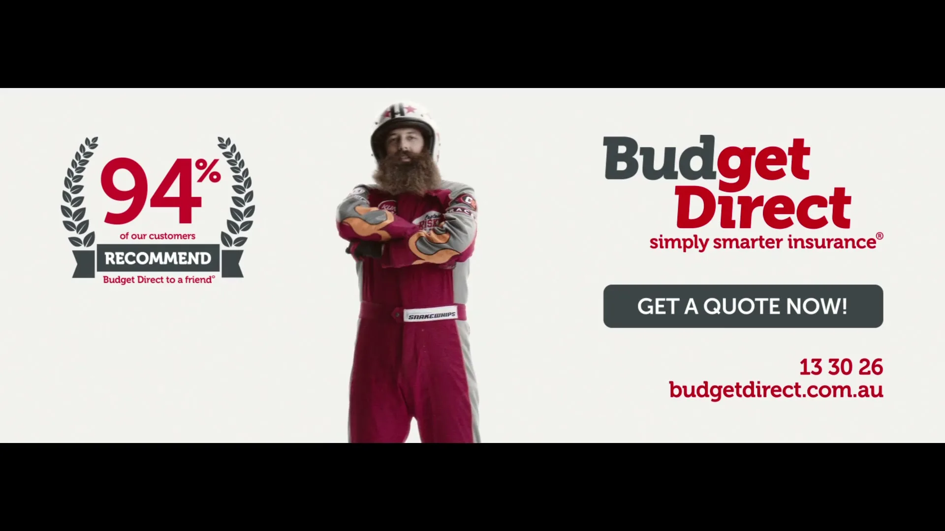 A man with a long beard and a racing suit stands in a studio, with text and logos for Budget Direct on either side.