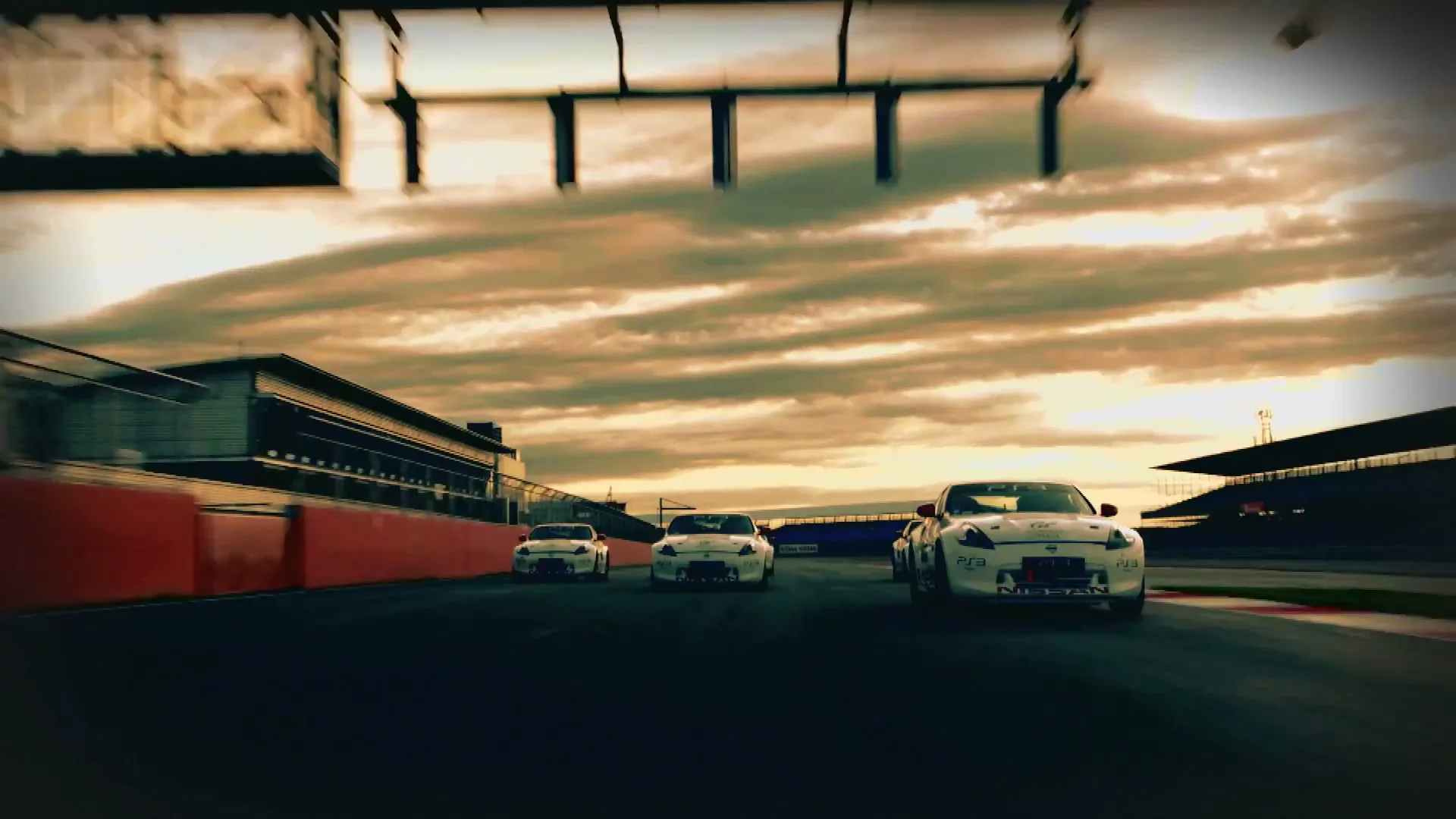 Three white Nissan race cars drive on a track at sunset, with a building and grandstands visible in the background.