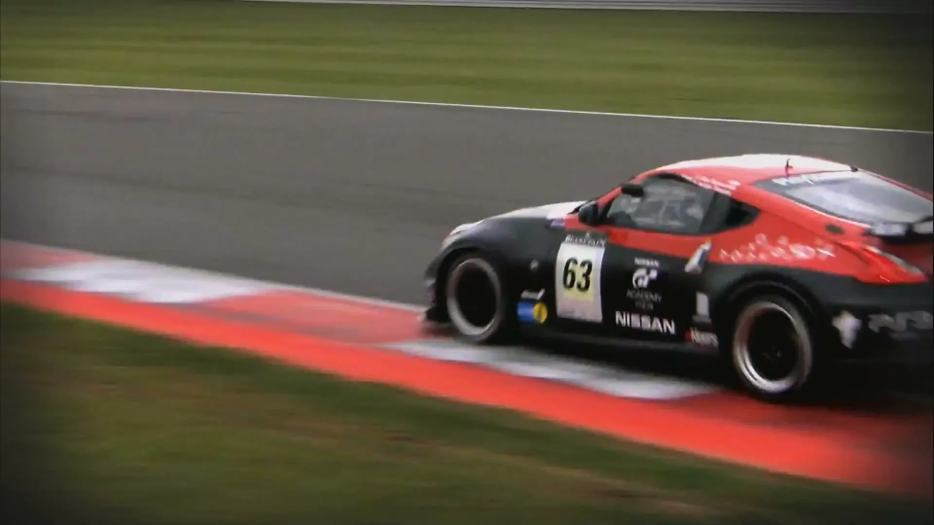 A black and red Nissan race car with the number 63 on its side speeds around a track on a cloudy day.