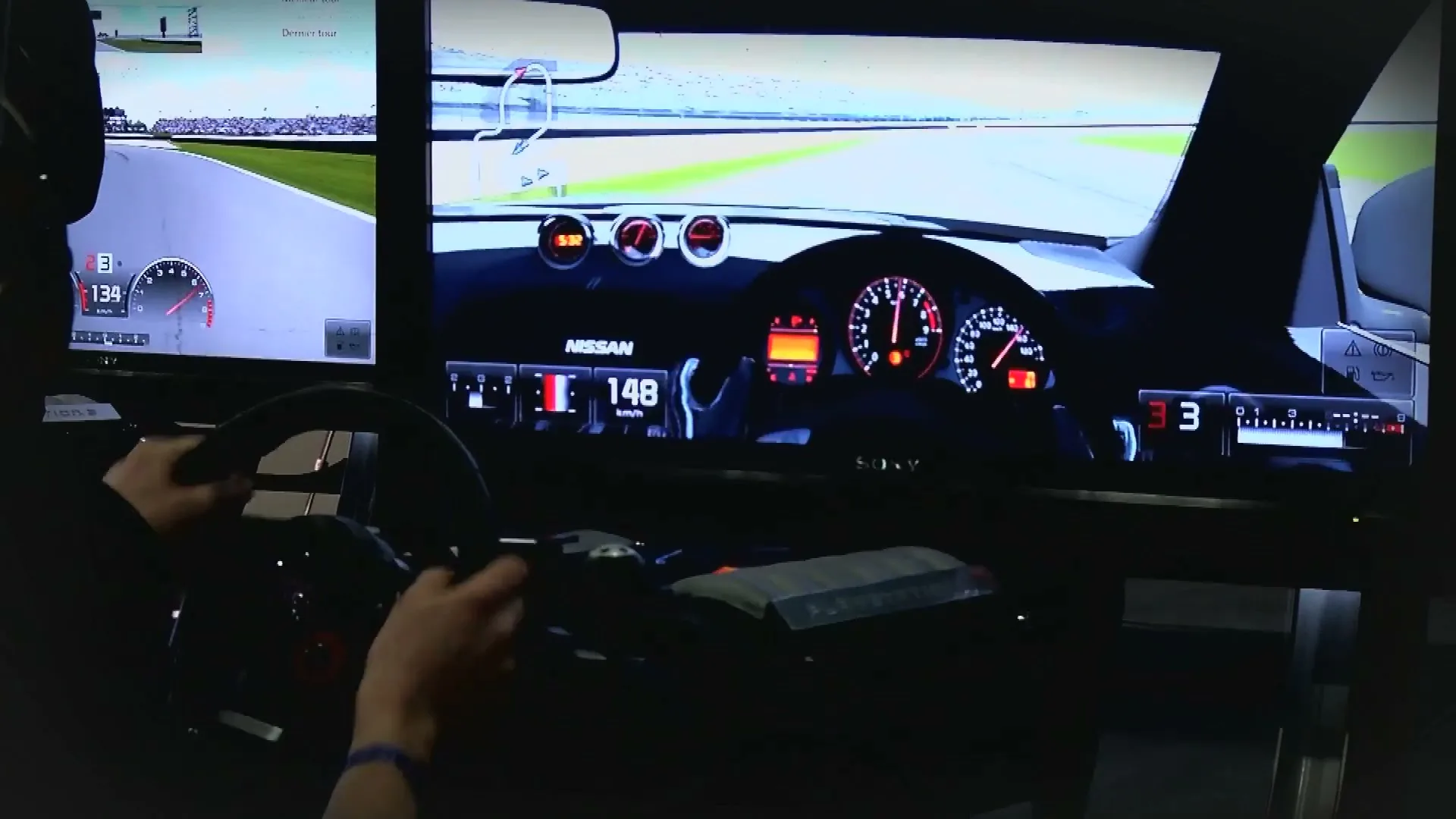 A person's hands grip a racing wheel, playing a car racing video game on multiple screens in a dark room.