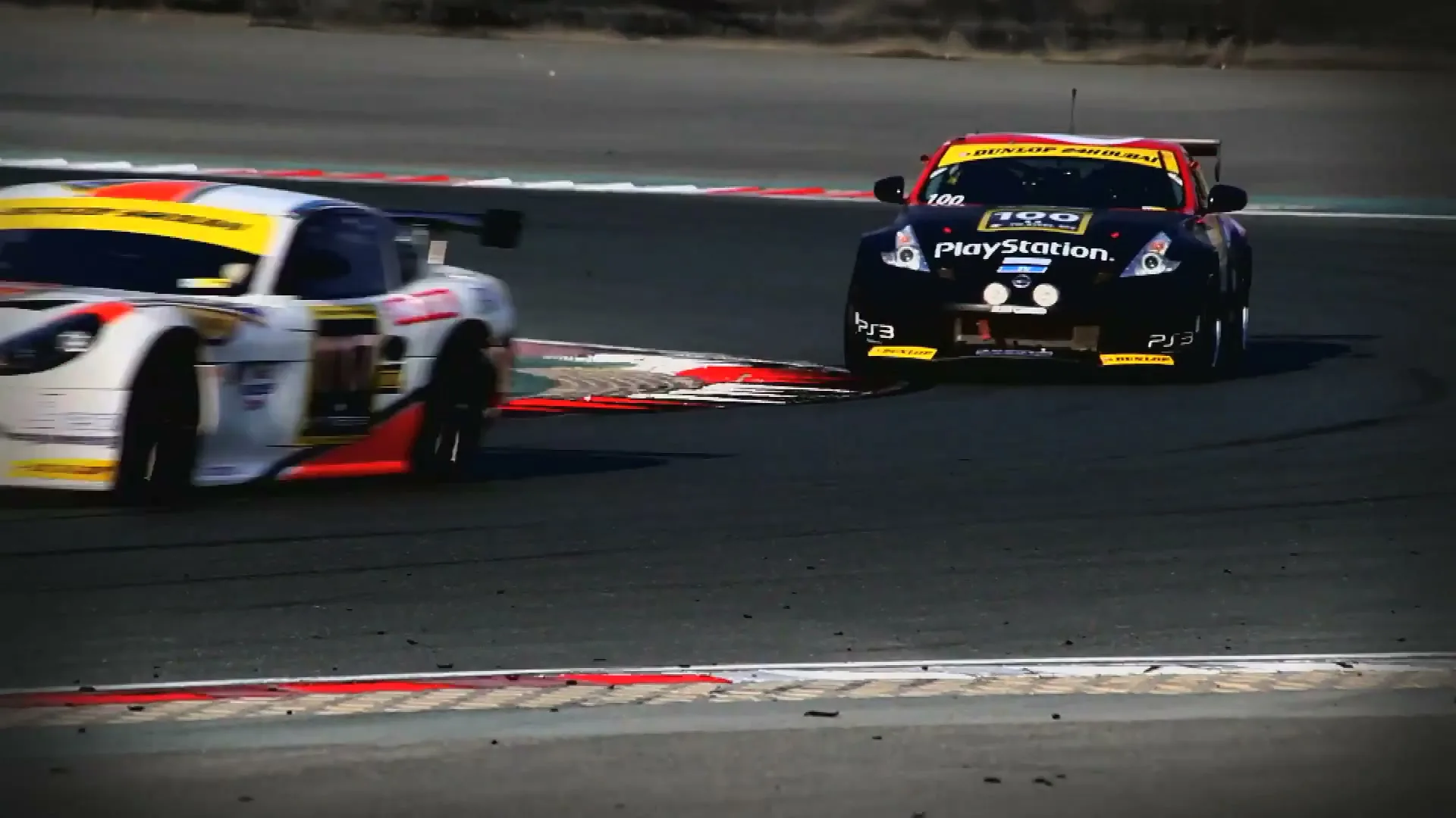 Two race cars, one white and one black, speed around a sharp turn on a race track during a bright day.