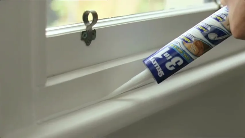 A person's hand applies Selleys 3 in 1 sealant to a white window frame, sealing a gap with a smooth bead of caulk.