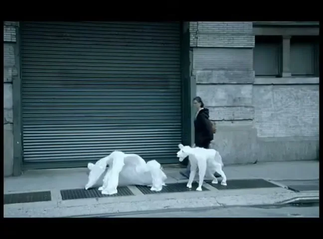 A yellow taxi drives past a woman walking on a city sidewalk, where two white, translucent polar bear figures are also present.