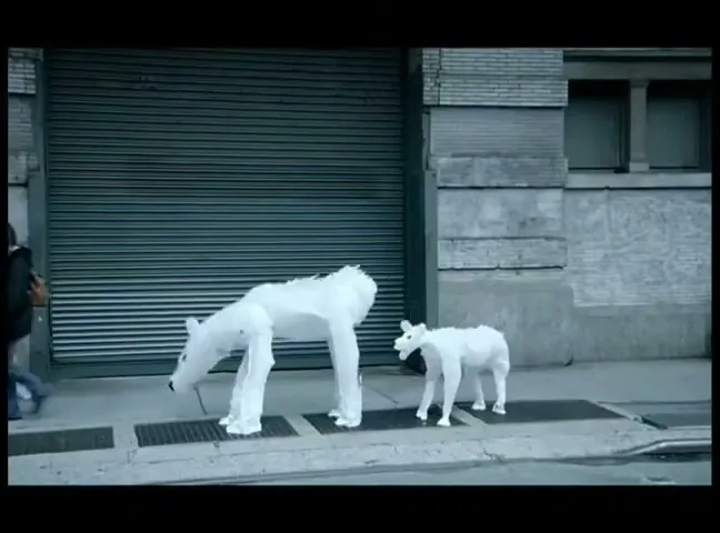 Two white, abstract polar bear figures, one large and one small, walk on a city sidewalk as cars and people pass by.