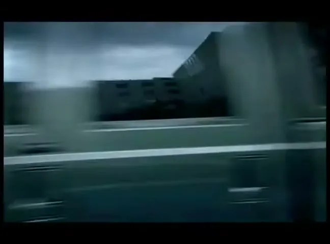 A blurry shot of a dark green car speeding past a building with a metal roll-down door, creating a sense of rapid movement.