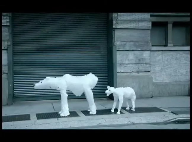 Two polar bears, one adult and one cub, made of white plastic bags, stand on a city sidewalk as a dark car drives past them.