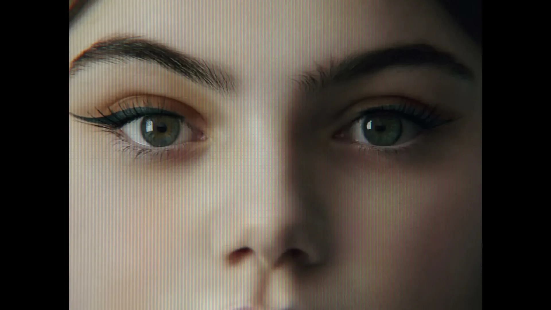 A young woman's face is seen in a closeup, with her eyes looking directly at the camera, as she removes her eyeliner.