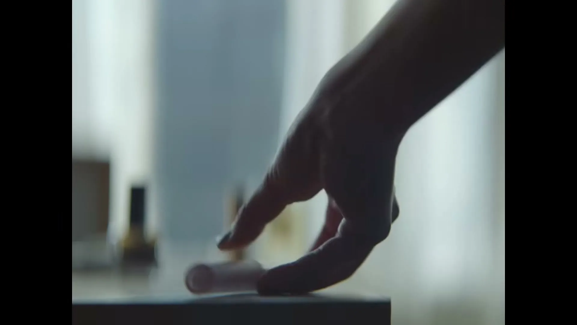 A young woman's hand reaches for a pink lipstick on a dresser in a bedroom.