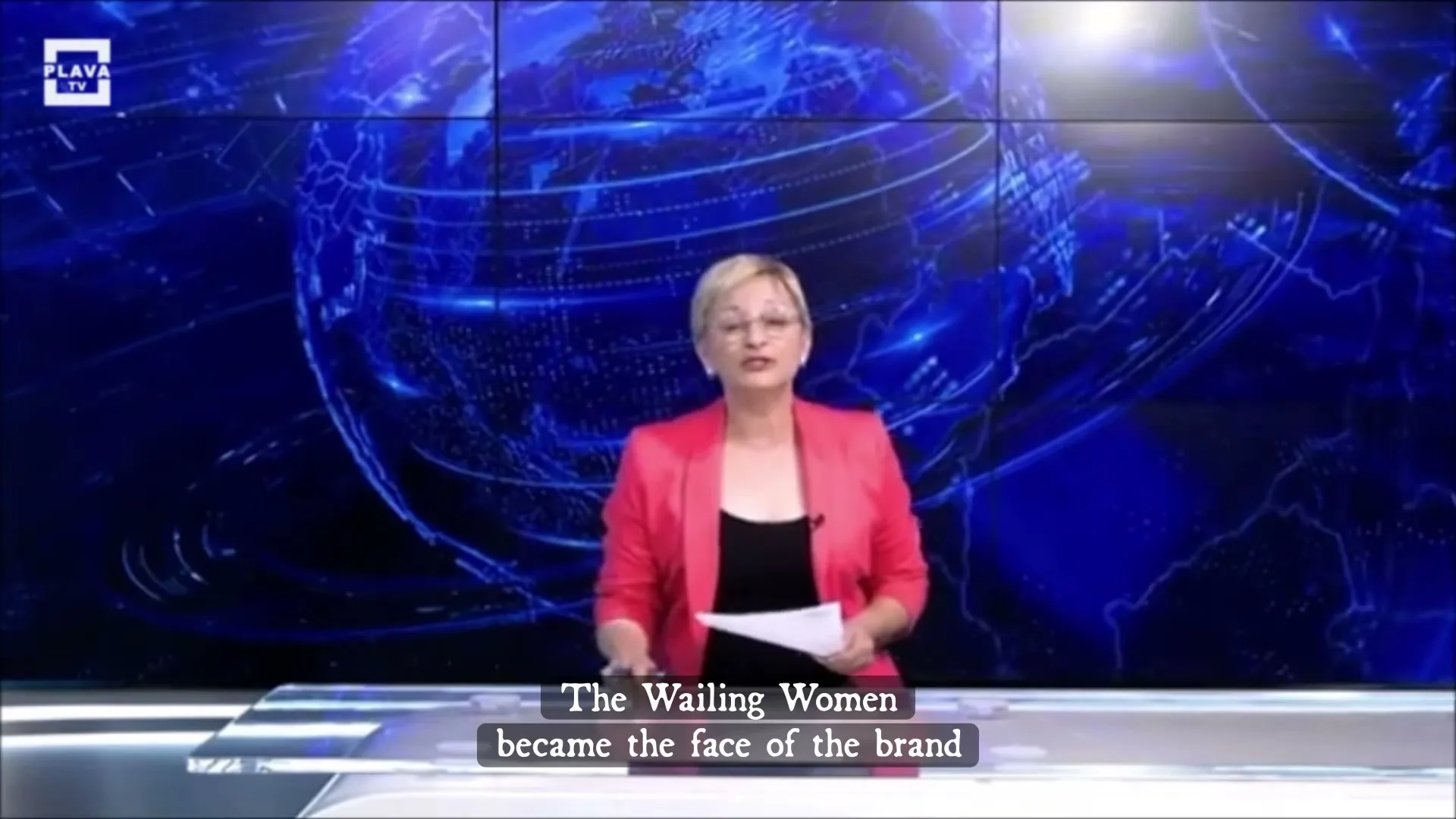 A female news anchor in a pink blazer reports from a studio with a large screen displaying a globe and a split screen showing a person on a bicycle.