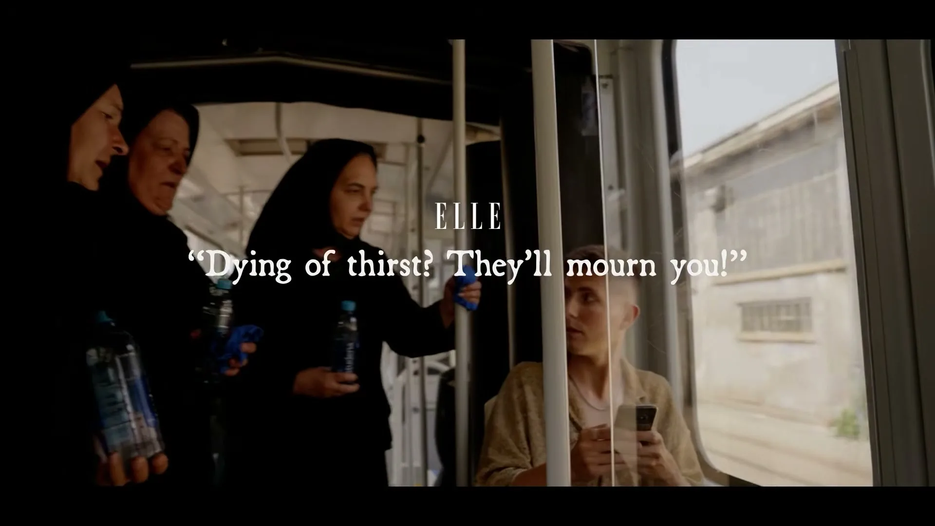 A young person on a tram looks up from their phone as three women in black robes and head coverings, holding water bottles, look at them with concern.