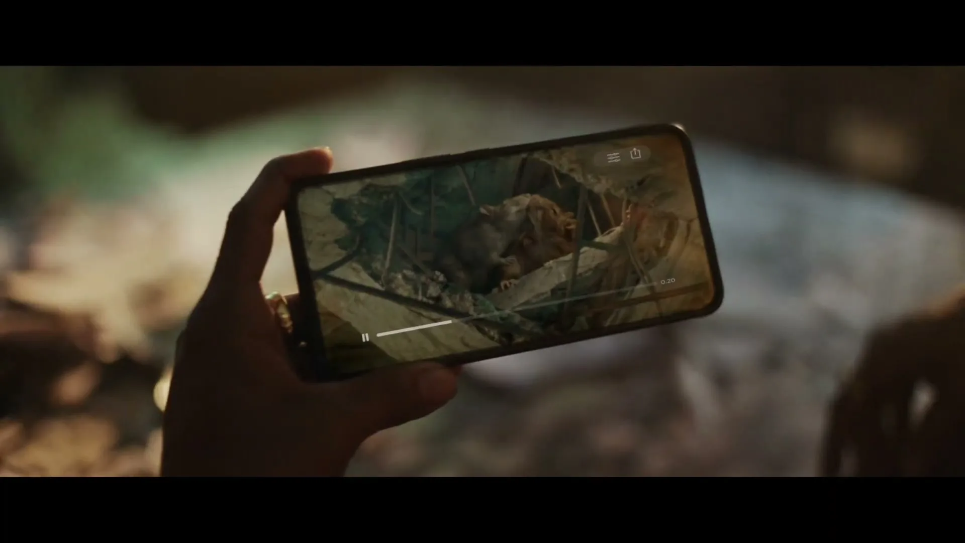 A person holds a smartphone horizontally, displaying a video of a small animal trapped in a cage, with a play bar visible on the screen.