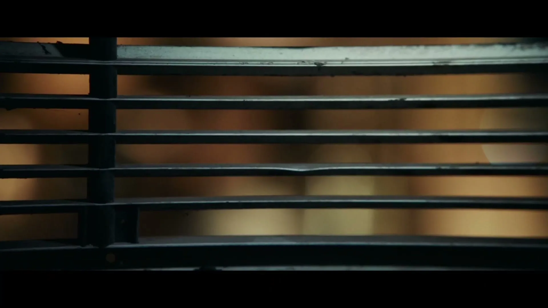 A close-up shot of venetian blinds, with a blurry, warm-toned background, suggesting an interior setting at night.