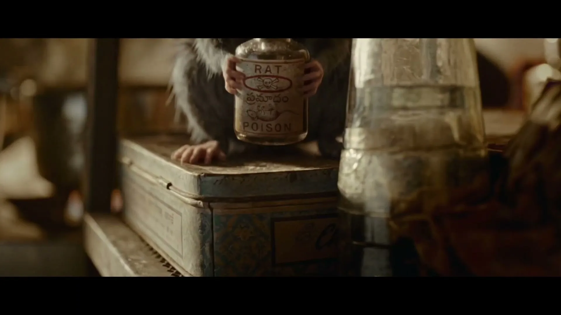 A small, furry rat with tiny paws holds a bottle labeled "RAT POISON" on a dusty, ornate metal box in a dimly lit interior.