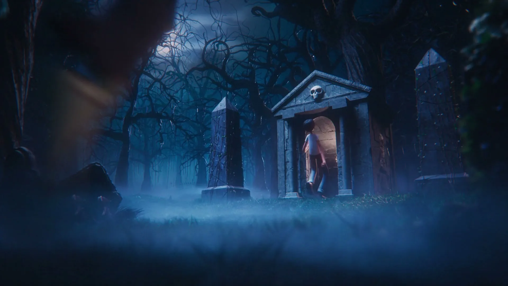 A young boy with a lantern walks into a spooky mausoleum in a dark, foggy graveyard at night, as a monster's legs walk past the camera.