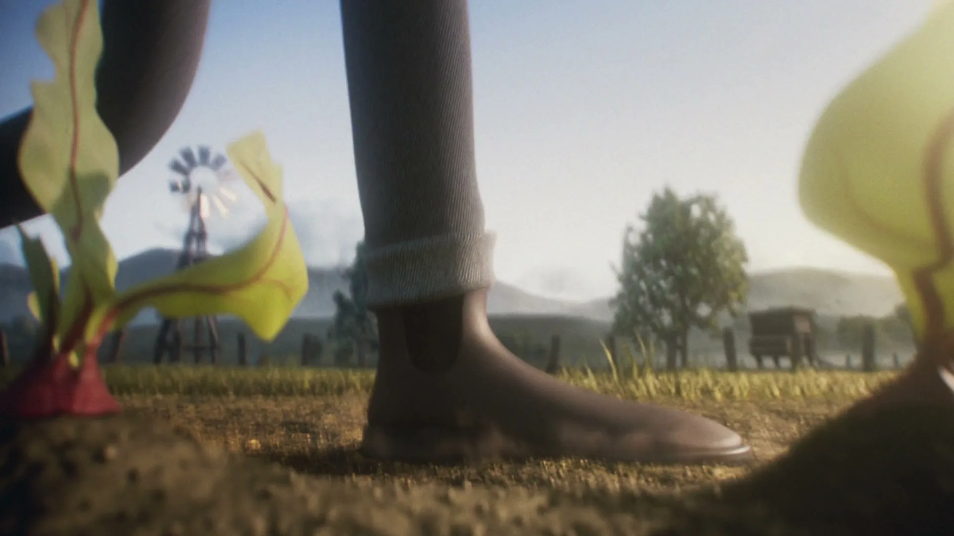A person's leg and foot in a boot walk through a field of growing plants, with a windmill and trees in the background.