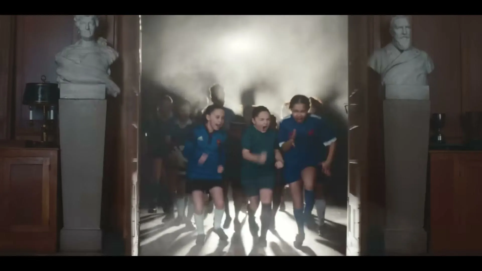 A wooden double door with dark glass panels opens to reveal a group of young female rugby players running out of a smoky, brightly lit doorway.