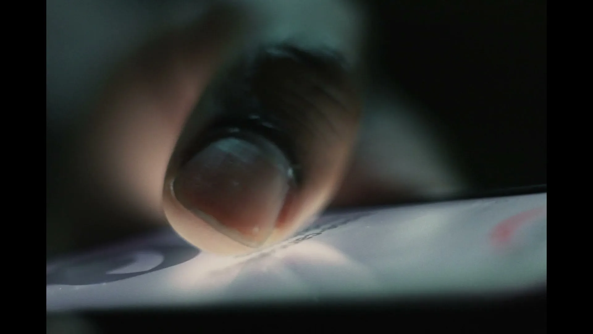 A person's finger taps on a smartphone screen, illuminated by the screen's light in a dark setting.