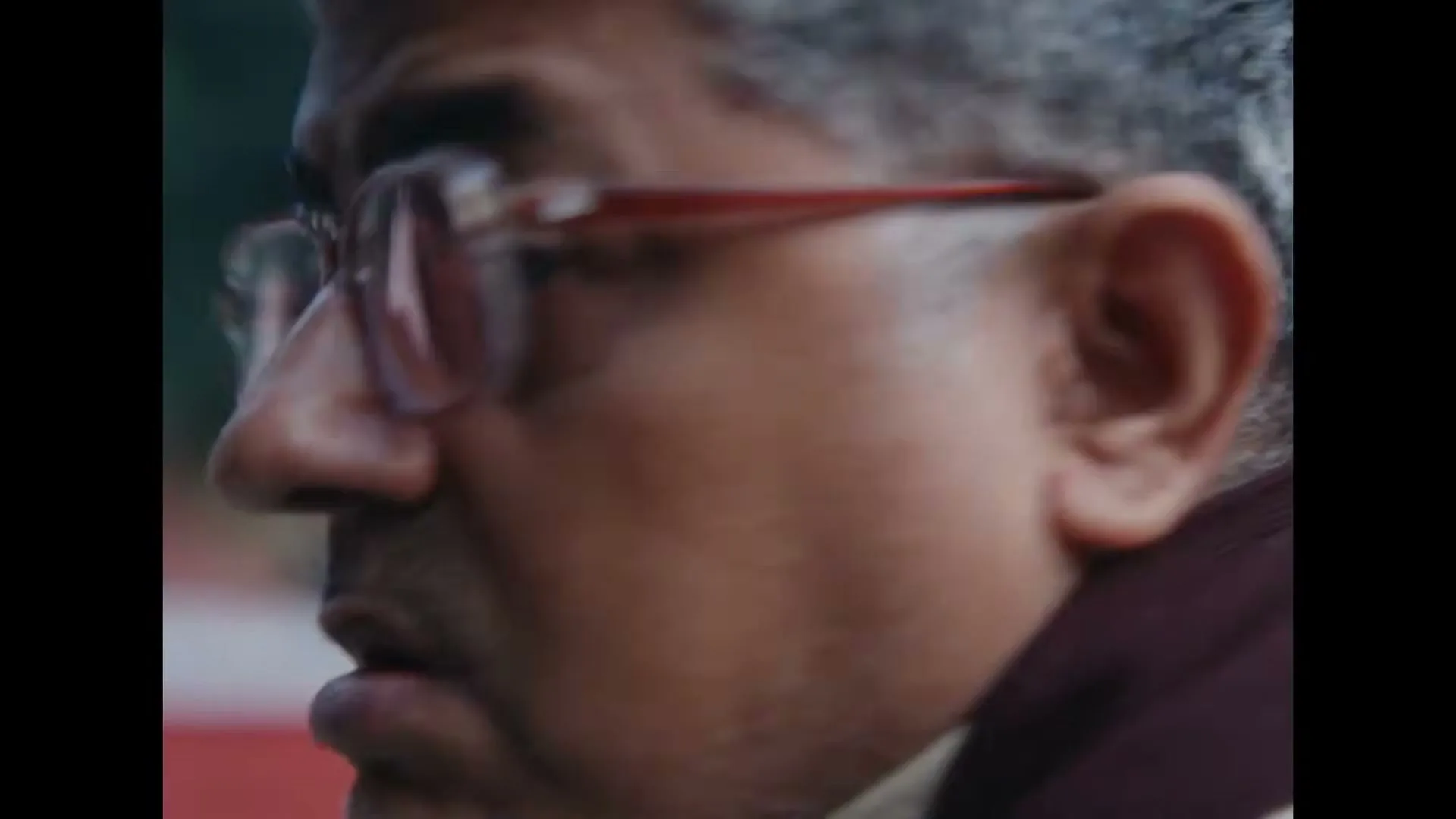 A middle-aged man with gray hair and glasses looks surprised as he turns his head to the camera in an outdoor setting.