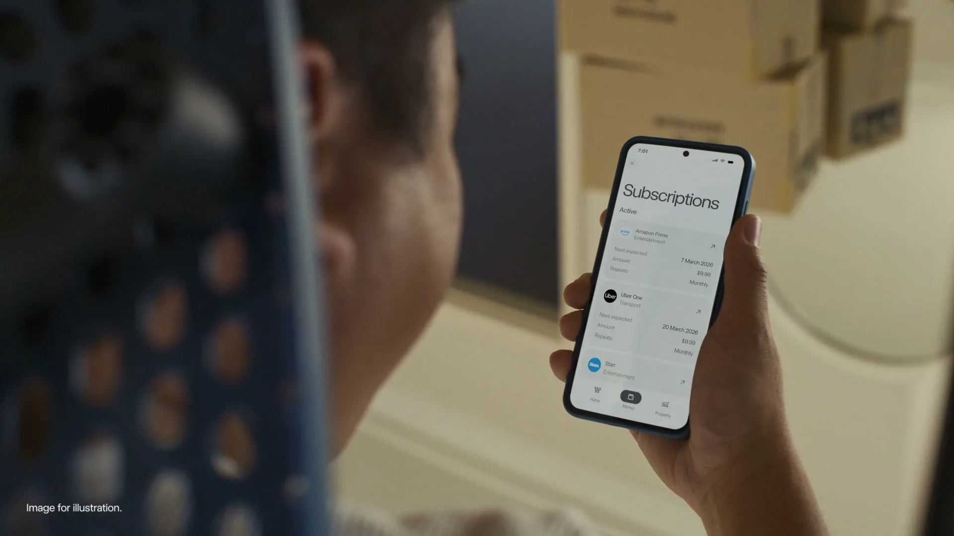 A man holds a smartphone displaying a "Subscriptions" screen, with a blurred background of moving boxes, in an interior setting.