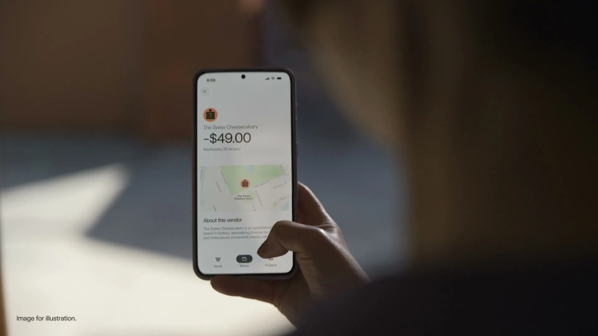 A person holds a smartphone, interacting with a banking app that displays a transaction and vendor details, in an interior setting.