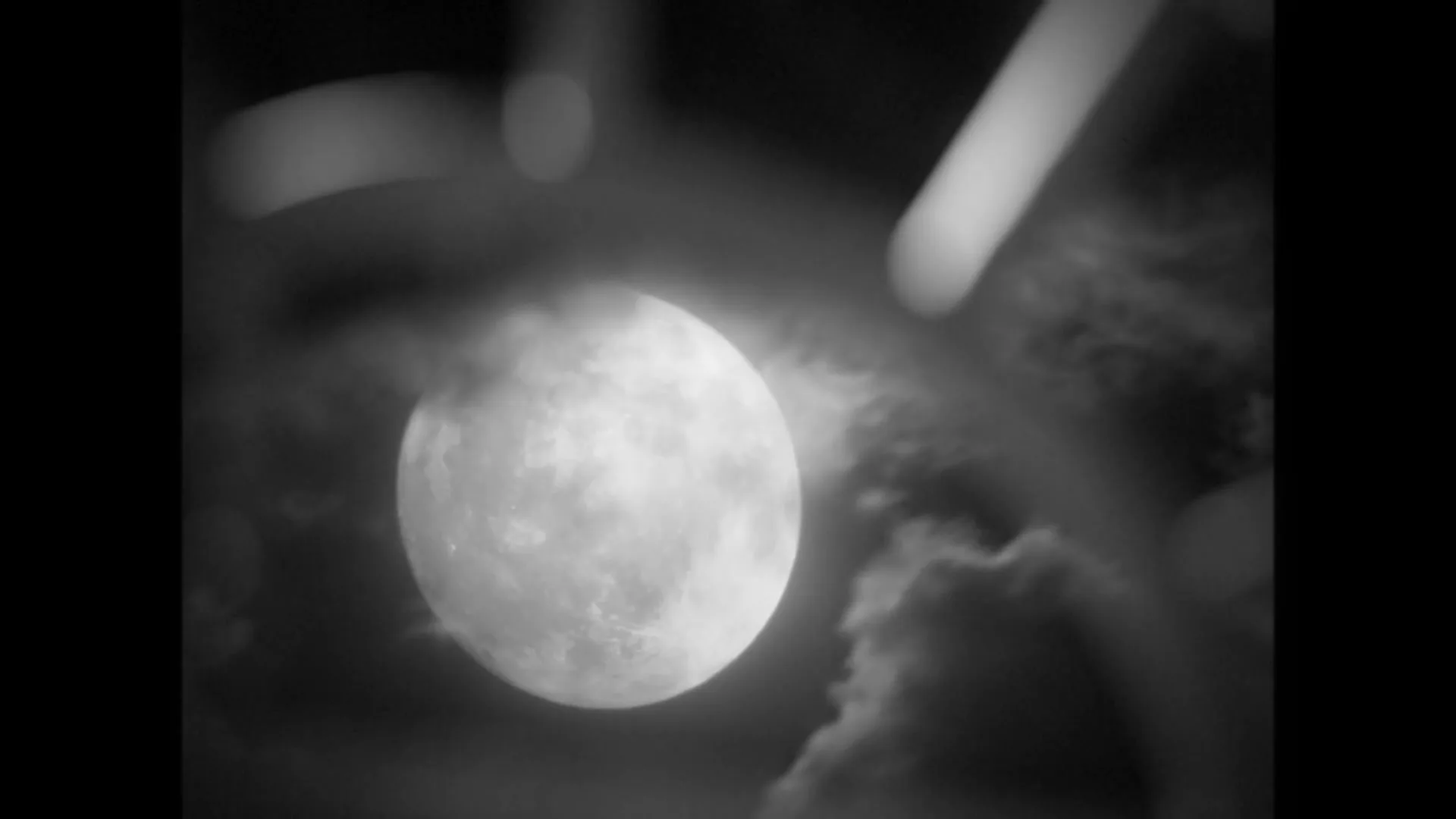 A full moon is seen through a blurry foreground, with clouds passing by in a black and white shot.