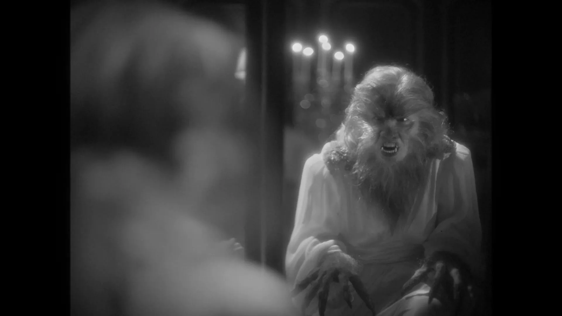 A woman with curly hair looks into a mirror, seeing a monstrous, hairy reflection of herself with fangs and claws in a dark room.