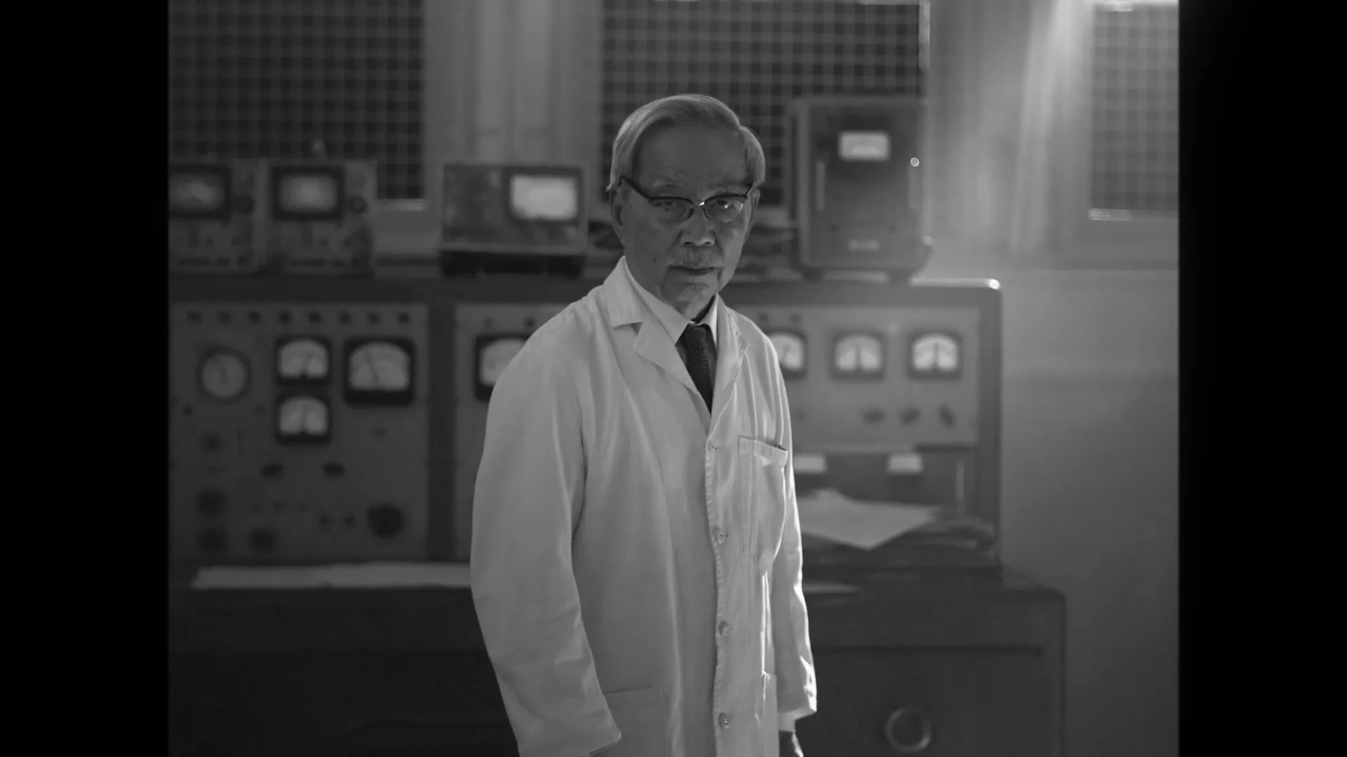 An older Asian man in a lab coat and glasses stands in a dimly lit, vintage-style laboratory, looking directly at the camera.