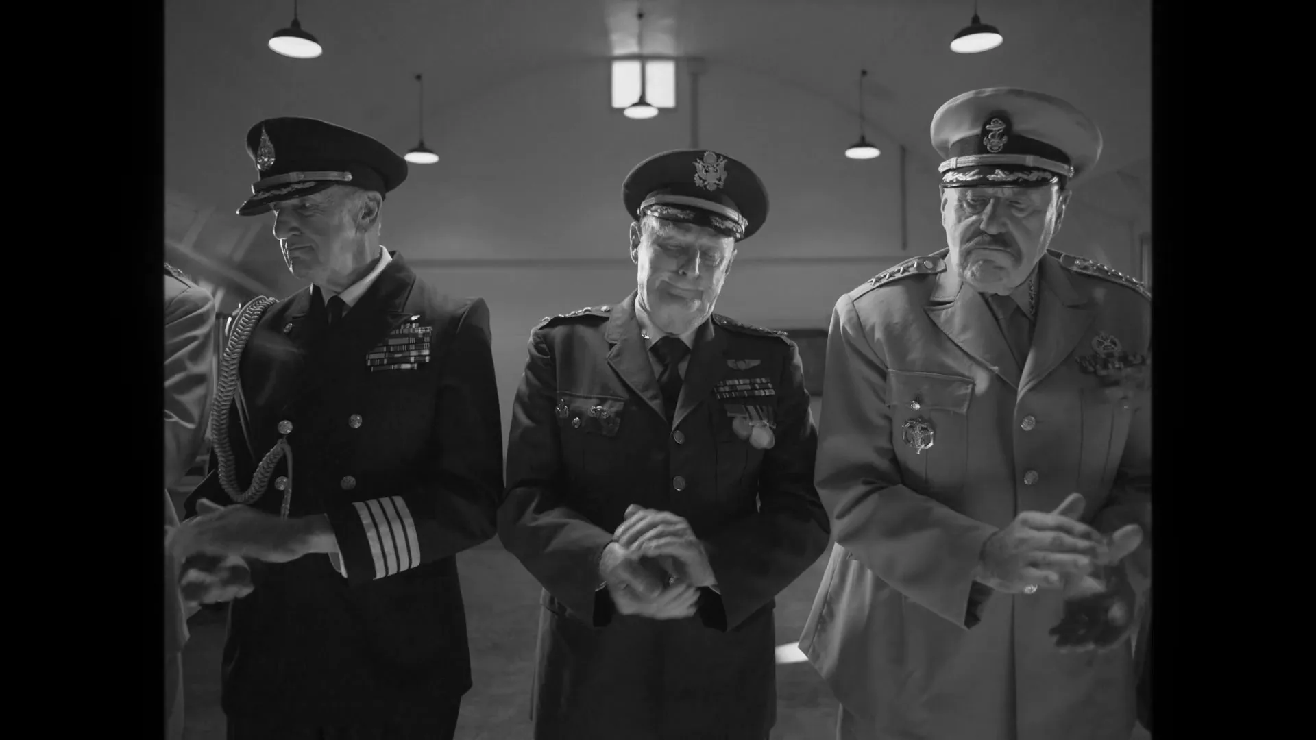 A group of seven military officers in uniform stand in a line, clapping, in a large hangar.
