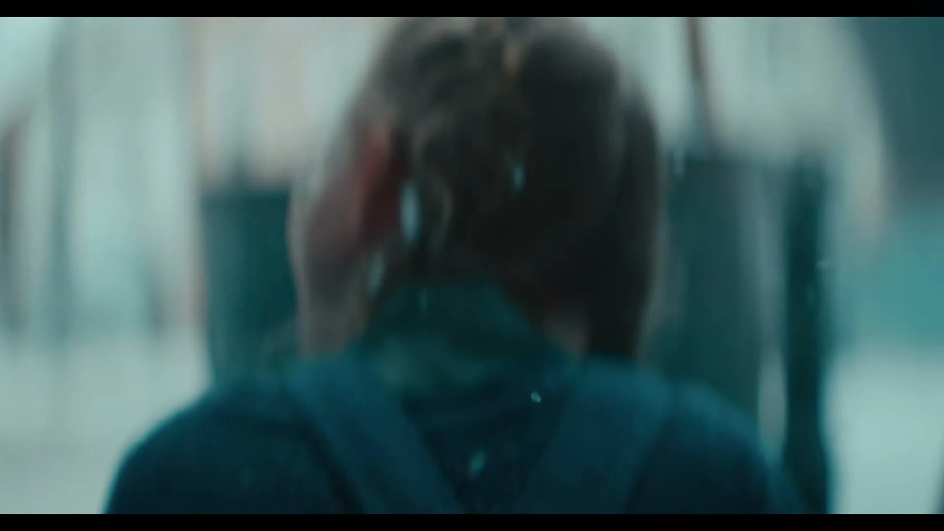 A blurry shot of a person's back, with light brown hair and a dark blue top, seen through a translucent, possibly watery, medium.