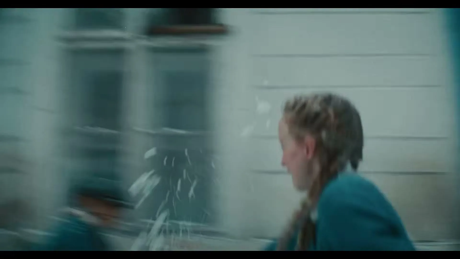 A young girl with blonde braids, wearing blue overalls, runs joyfully while throwing snowballs on a snowy street.