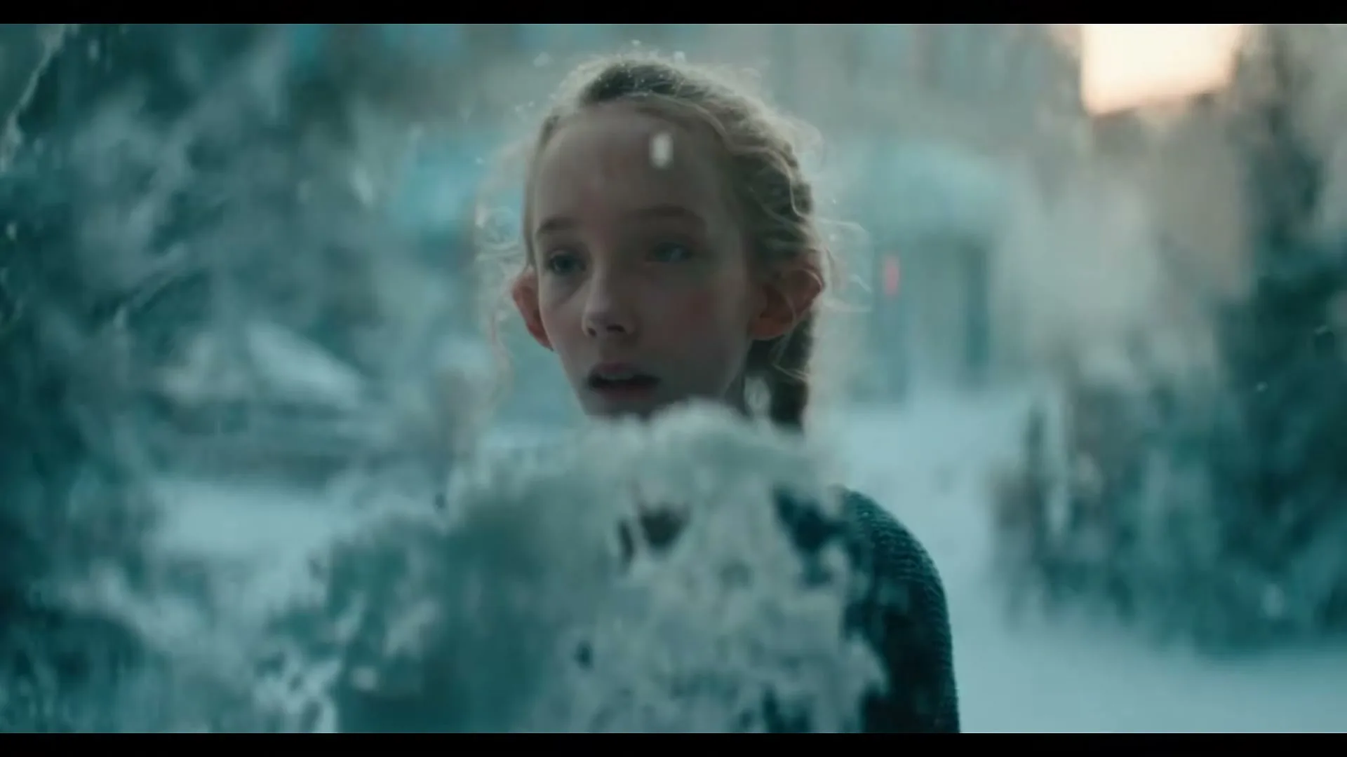 A young girl with braided hair looks surprised as snow falls around her in a wintery outdoor setting.