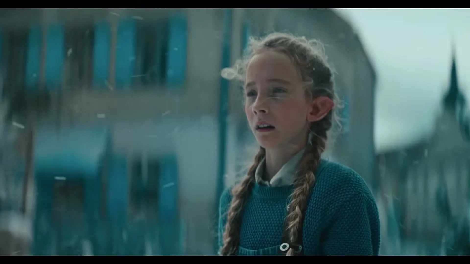 A young girl with braided hair and elf ears looks concerned as snow falls around her in a European village.