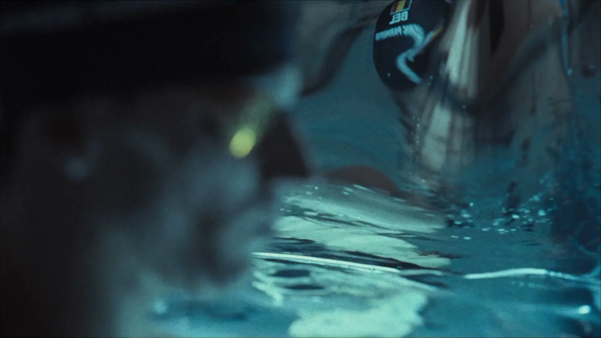 A swimmer with a black cap featuring the Belgian flag and "BEL" is seen from a low angle, partially submerged in a pool.